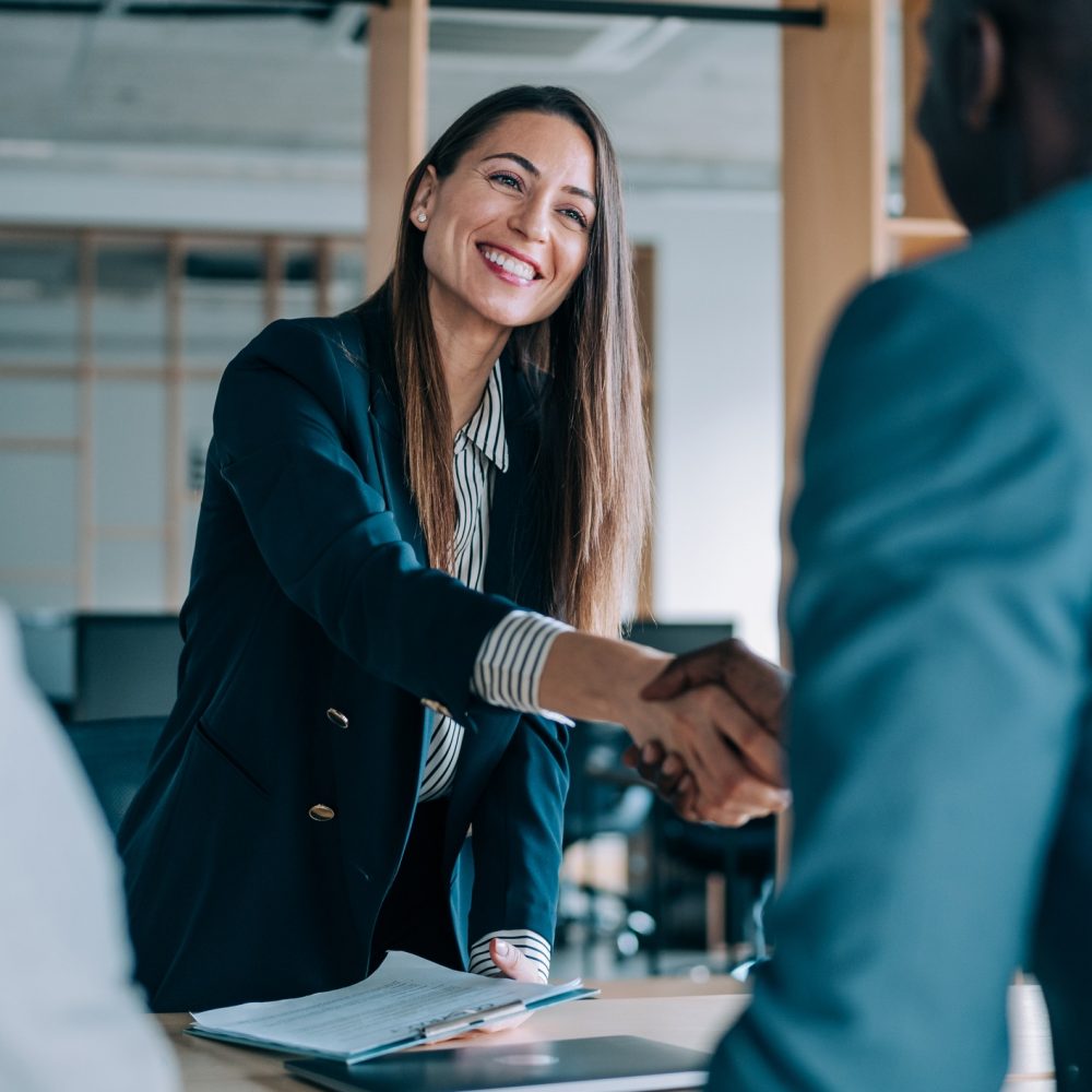 Business people shaking hands in the office. Group of business persons in business meeting. Three entrepreneurs on meeting in board room. Corporate business team on meeting in modern office. Female manager discussing new project with her colleagues. Company owner on a meeting with two of her employees in her office.